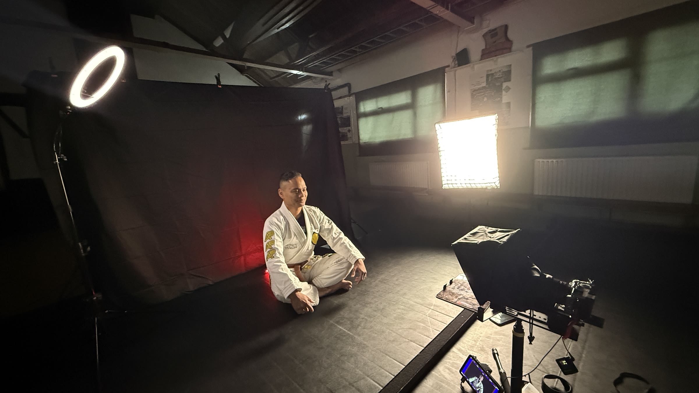 Coach in a gi seated in front of the backdrop during filming