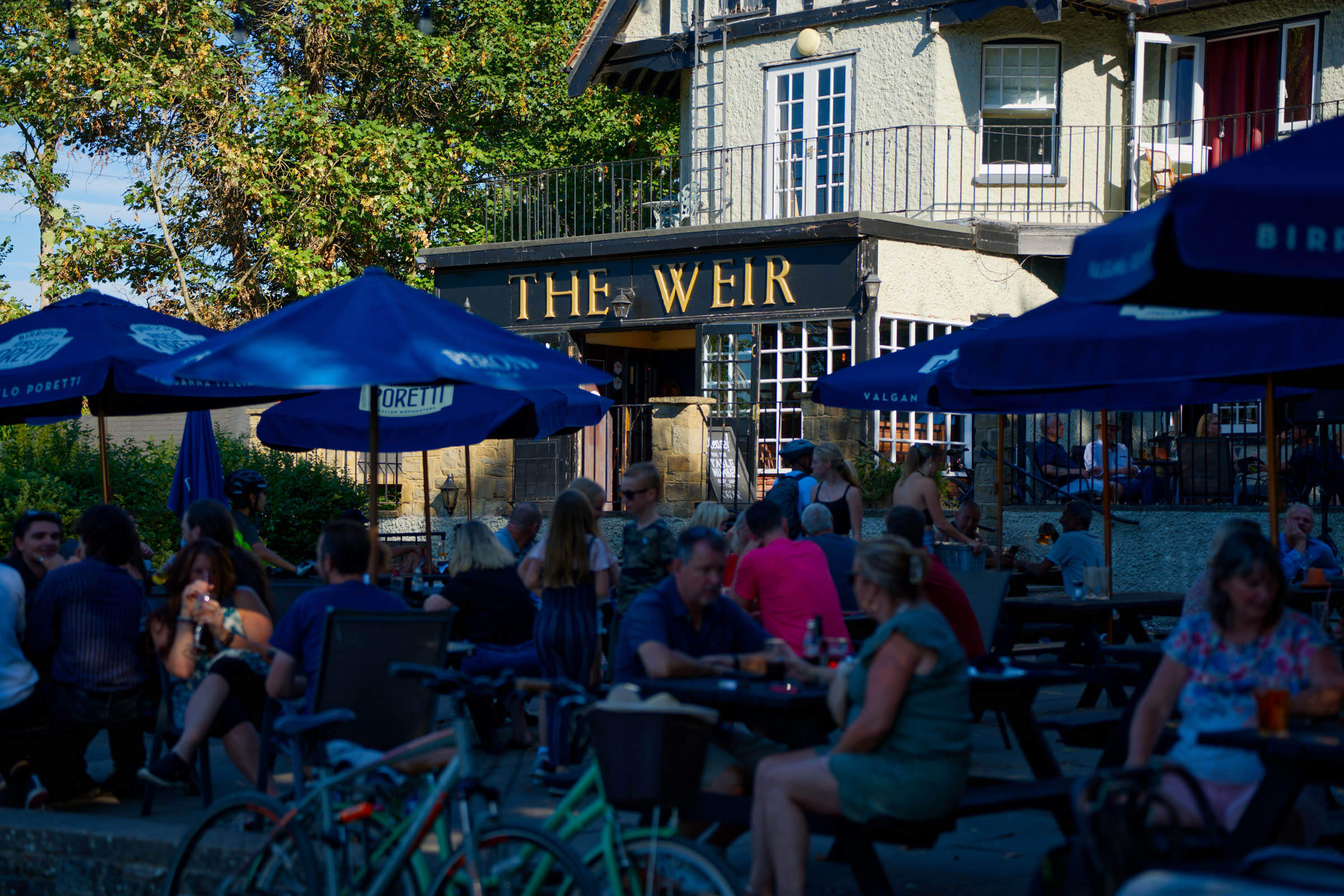 Guests filling the riverside terrace outside The Weir on a sunny afternoon