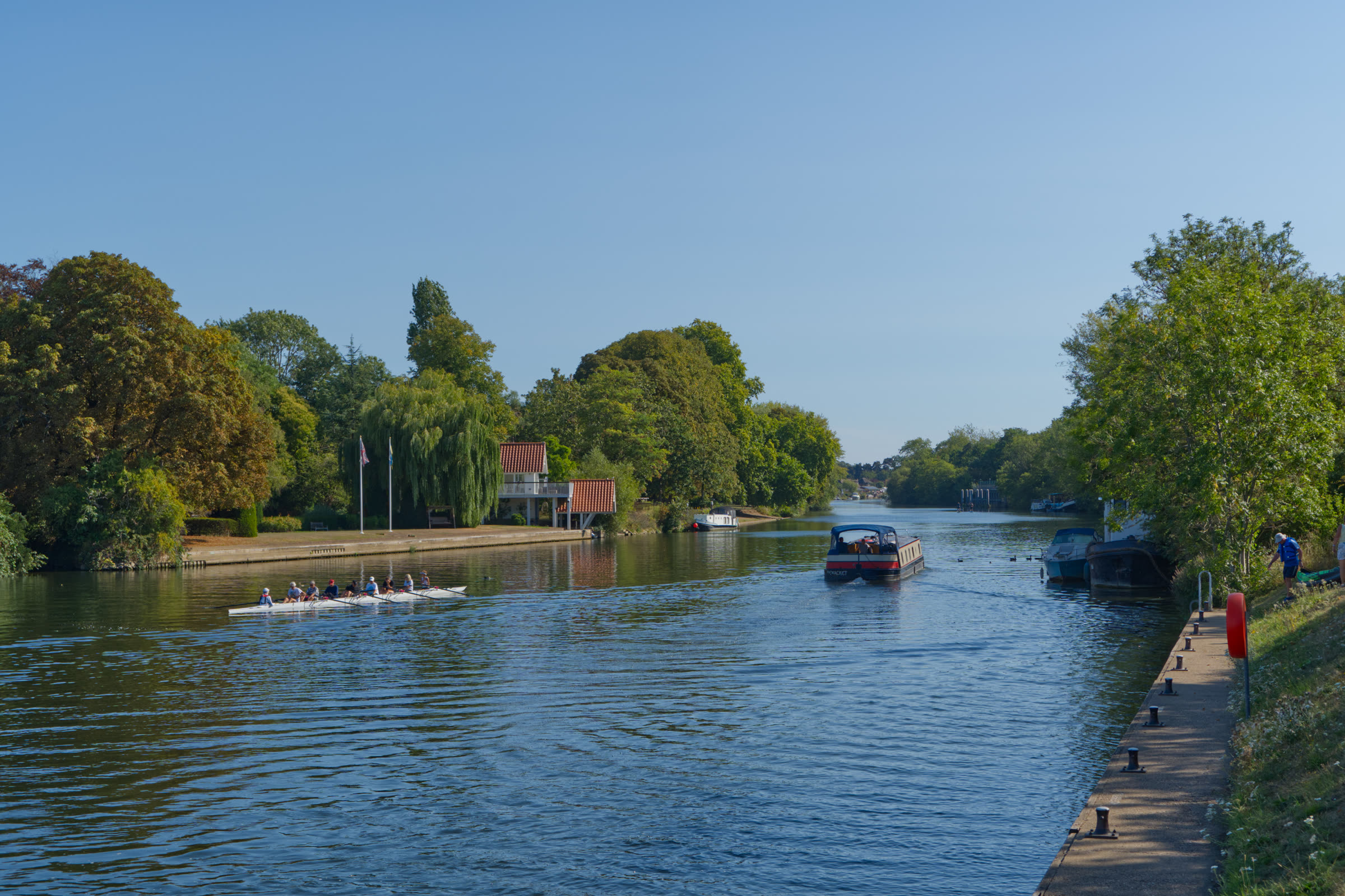 Rowing crew and a narrowboat sharing the river on a clear day