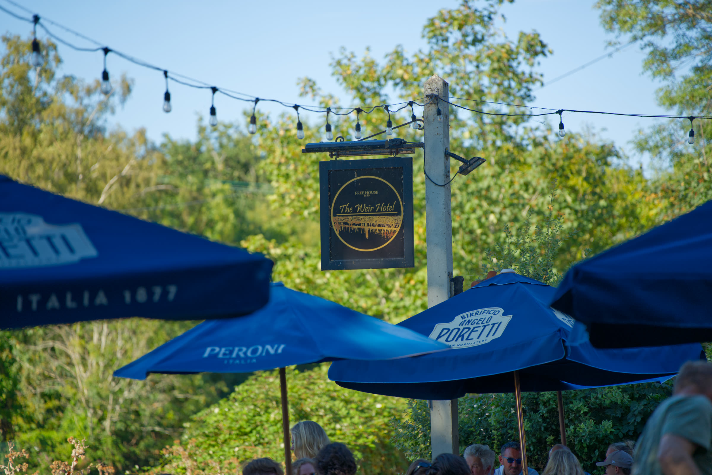 The Weir Hotel hanging sign framed by parasols and trees
