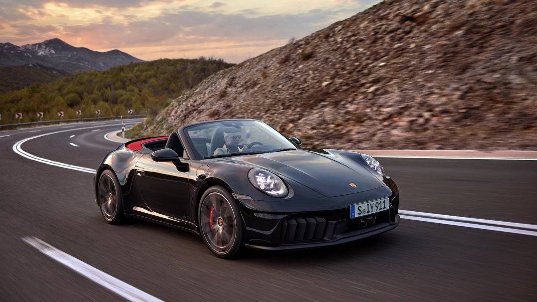 Black Porsche 911 cabriolet rolling shot on a coastal mountain road at sunset