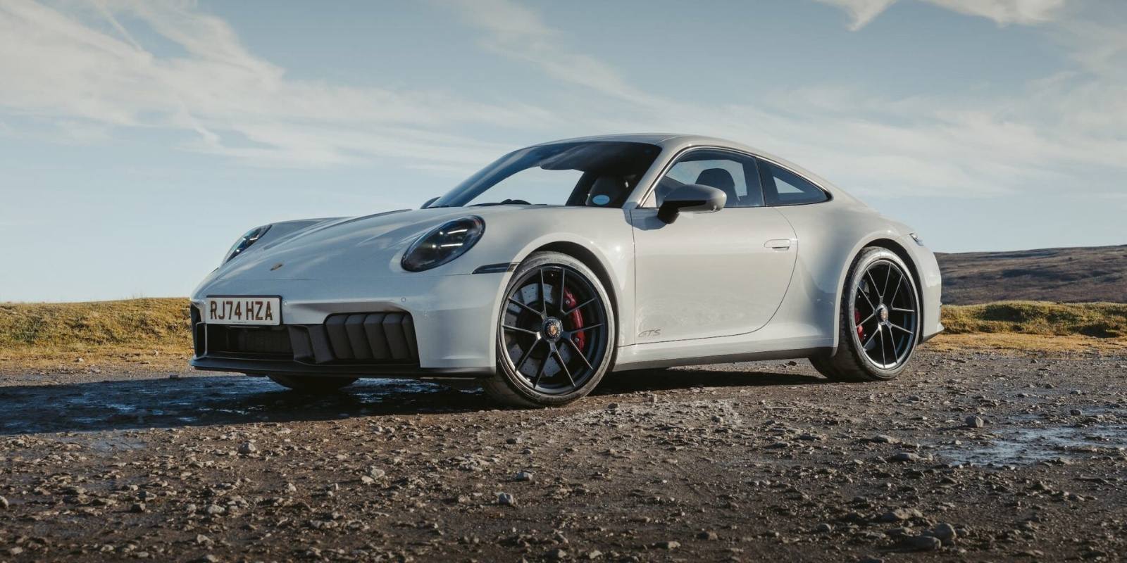 Grey Porsche 911 GTS parked on a gravel ridge under open sky